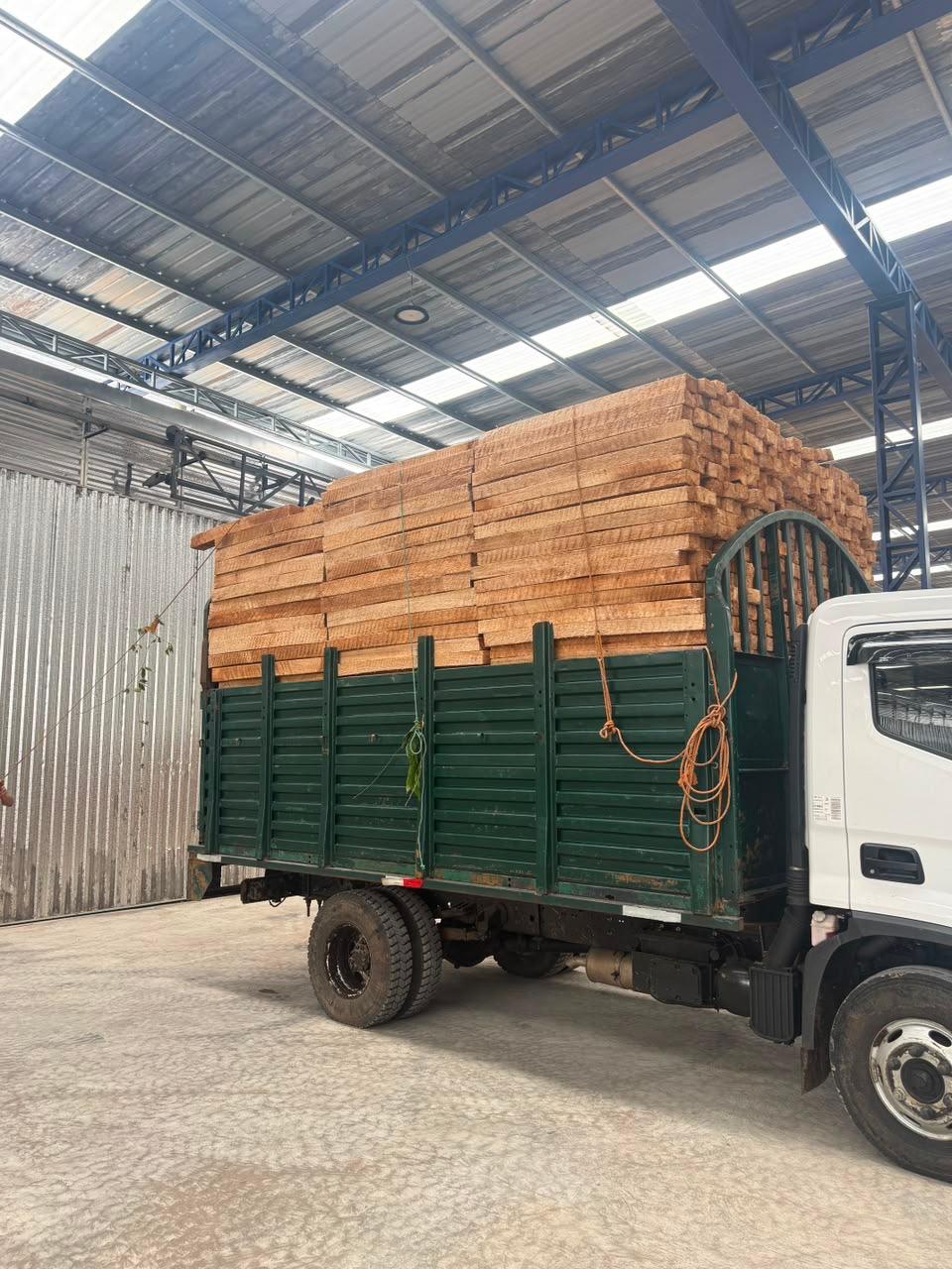 Camión cargado de madera escuadrada bajo una cubierta industrial.